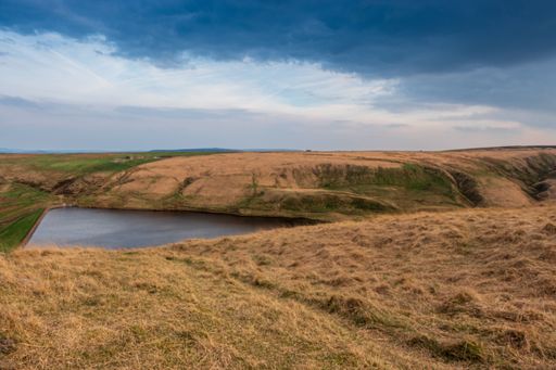 A small lake surrounded by dry grassy hills under a cloudy sky