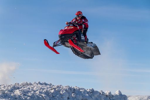 Snowmobiler jumping high above the track. On a snowmobile, a sportsman. It's a overcast day for a winter competition. Motorsports in the snow