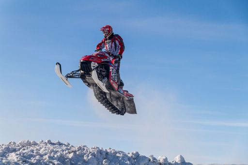 Snowmobiler jumping high above the track. On a snowmobile, a sportsman. It's a overcast day for a winter competition. Motorsports in the snow