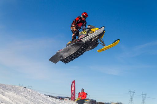 Snowmobiler jumping high above the track. On a snowmobile, a sportsman. It's a overcast day for a winter competition. Motorsports in the snow