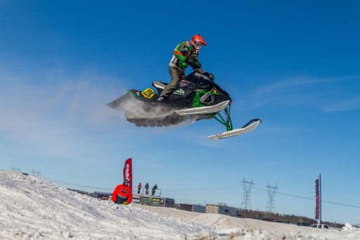 Snowmobiler jumping high above the track. On a snowmobile, a sportsman. It's a overcast day for a winter competition. Motorsports in the snow
