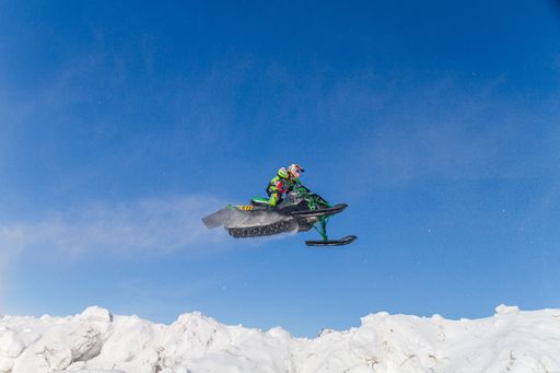 Snowmobiler jumping high above the track. On a snowmobile, a sportsman. It's a overcast day for a winter competition. Motorsports in the snow
