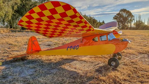 An old, orange radio control airplane on a field at sunset
