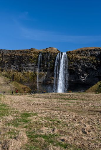 A vertical shot of the Seljalandsfoss waterfall with a clear blue sky in Iceland