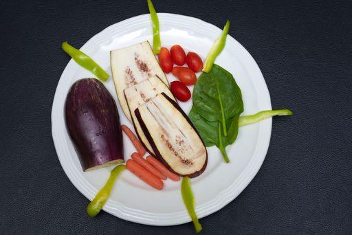 A closeup shot of a plate filled with eggplants, tomatoes, green beans and spinach on a black surface