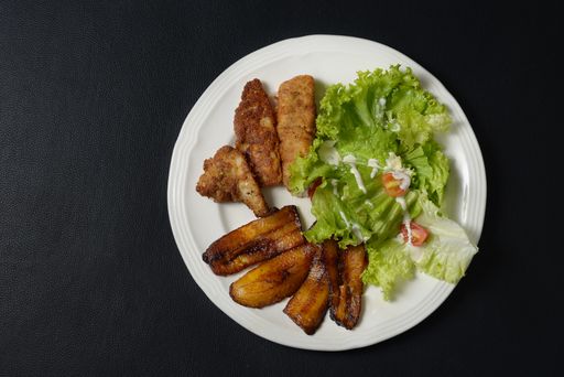 A top view of fried vegetables with salad in a white plate on a black surface