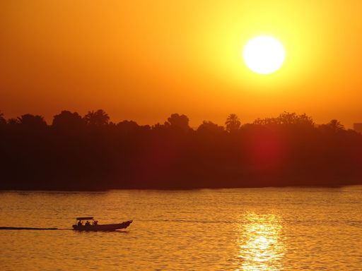 A small boat cruising on a calm coast against the silhouette of forest and bright sunset