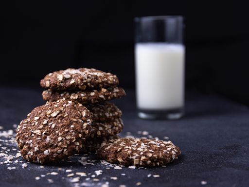 A closeup shot of chocolate oat biscuits and a glass of milk on a black background