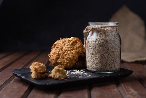 A selective focus shot of a black plate with oat cookies and a glass jar with uncooked oats on a wooden surface