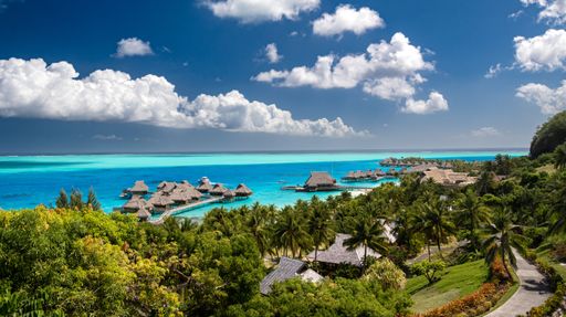 An aerial view of Conrad Bora Bora Nui hotel with overwater bungalows under a blue cloudy sky
