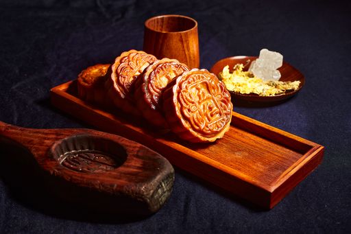 A closeup shot of traditional Chinese mooncakes served on a wooden tray on a dark blue tablecloth