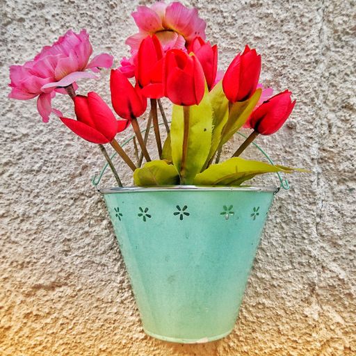 A closeup shot of red and pink flowers in a green basket hanging on a wall as a decoration