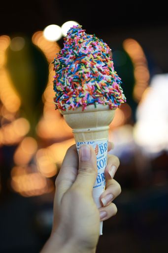A vertical selective shot of a person holding an ice cream waffle cone with sprinkles