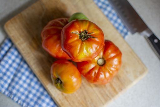 An overhead selective shot of tomatoes stacked on each other on a wooden chopping board