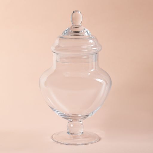 A closeup shot of a decorative glass jar with a lid perfect for holding snacks on a light pink background