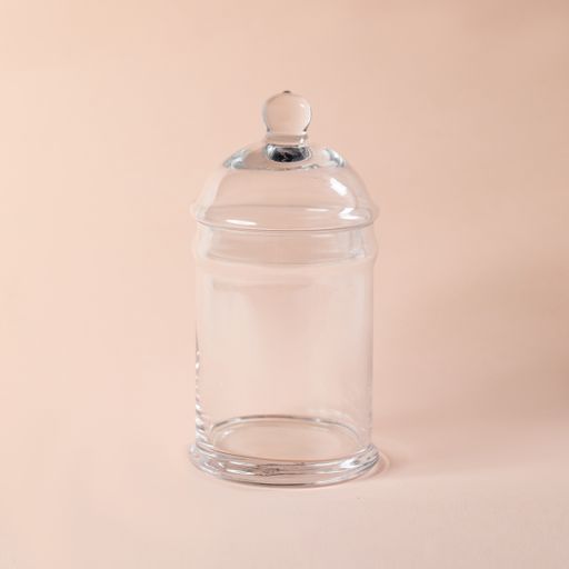 A closeup shot of a decorative glass jar with a lid perfect for holding snacks on a light pink background