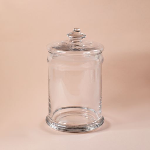 A closeup shot of a decorative glass jar with a lid perfect for holding snacks on a light pink background