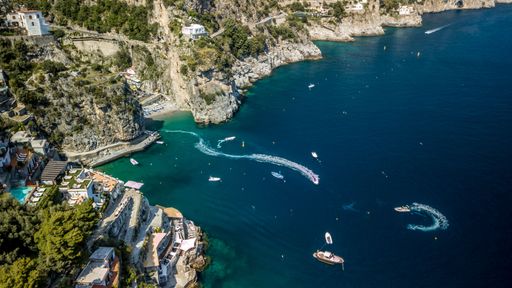 An aerial view of the blue sea against rocky Amalfi coast covered with greenery and buildings in Italy