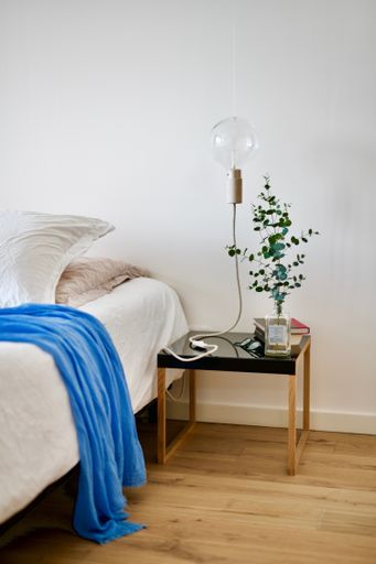 A vertical shot of a modern artsy bed lamp on a black table beside a bed. Perfect for room decor.