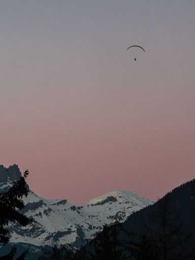 A vertical shot of the snow capped Mont Blanc and a paraglider against a sunset sky in France