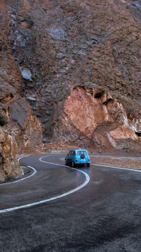 A back view of old car driving in a narrow Moroccan road surrounded by cliffs