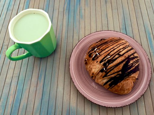 yummy breakfast combo, with iced shaken matcha latte and a chocolate croissant, on a distressed wooden blue table