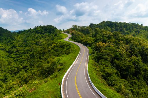 A mesmerizing aerial view of a narrow road in the middle of green forested hills on a sunny day