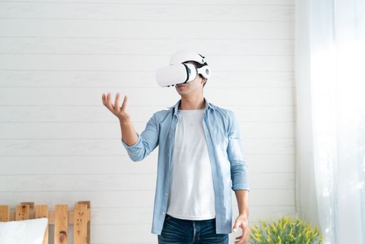 A young Thai man in a VR headset enjoying a virtual reality experience in a white bedroom
