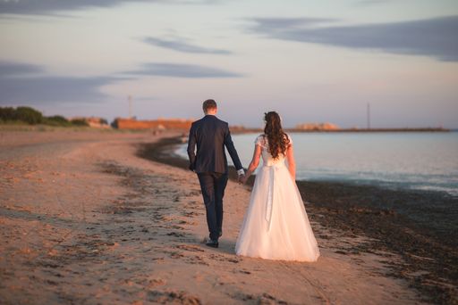 A back view of a beautiful bride and groom holding hands and walking on a beach