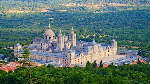 The aerial view of the Royal Seat of San Lorenzo de El Escorial surrounded by trees on a sunny day