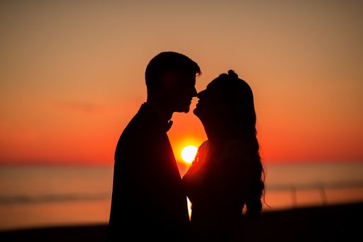 A silhouette of a bride and groom kissing on a beach at sunset