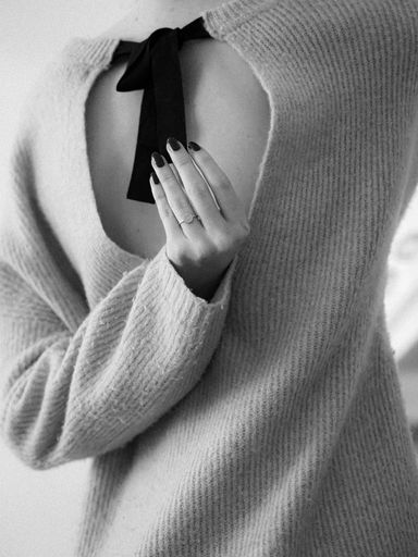 A young woman wearing a beige sweater with a cropped back against a white background