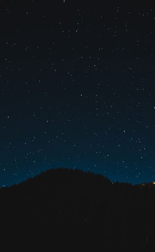 A silhouette of a mountain with trees under the beautiful sky with a lot of stars at night