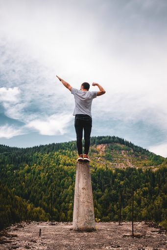 A vertical shot of a young male posing on a platform surrounded by hills under a cloudy sky at daytime