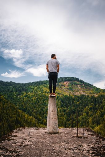 A vertical shot of a young male standing on a platform surrounded by hills under a cloudy sky