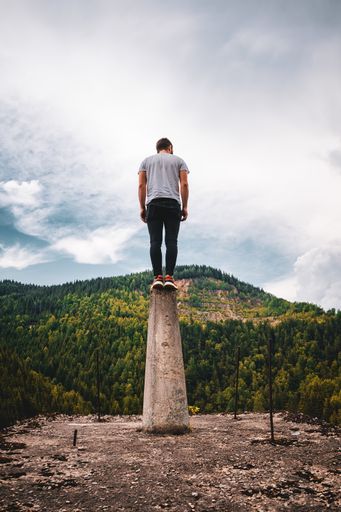 A vertical shot of a young male standing on a platform surrounded by hills under a cloudy sky