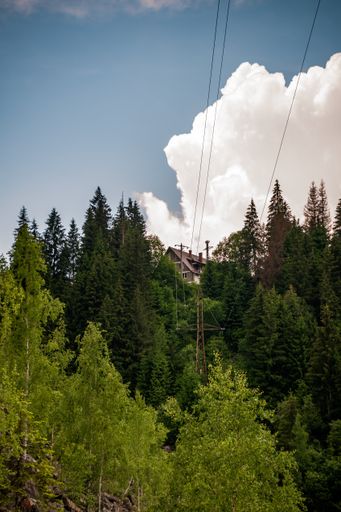 A vertical shot of hills covered in greenery under a blue cloudy sky and sunlight