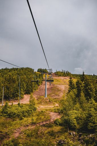 A vertical shot of chairlifts surrounded by greenery under a cloudy sky