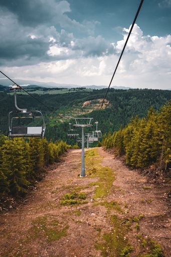 A vertical shot of chairlifts surrounded by hills covered in greenery under a cloudy sky