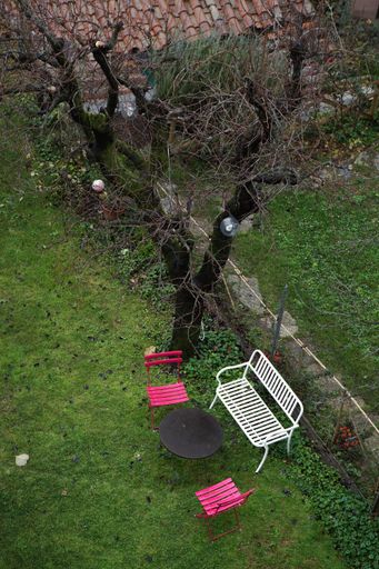 A vertical shot of a garden in a backyard with a white bench a round table and pink chairs