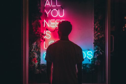 A cool shot of a male standing near "All you need is love" pink and blue neon signage