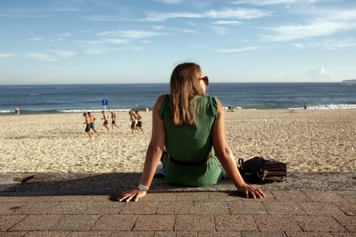 A caucasian female, wearing a green dress and sunglasses, sitting at Bondi beach, Sydney, Australia