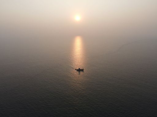Scenic view of the silhouette of small fishing boat on foggy lake during golden sunset reflected on surface of water