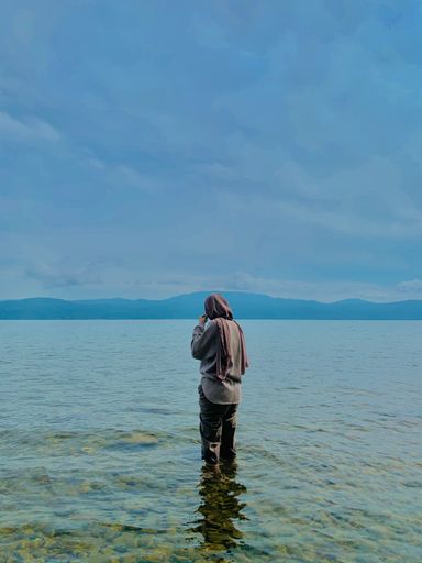 A girl with hijab standing in the sea and enjoying the moment under cloudy sky