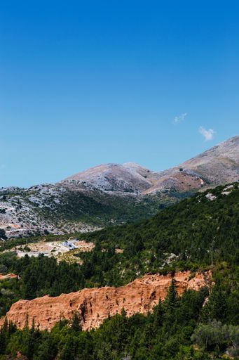 A vertical shot of green hills covered in lush forests under the clear blue sky