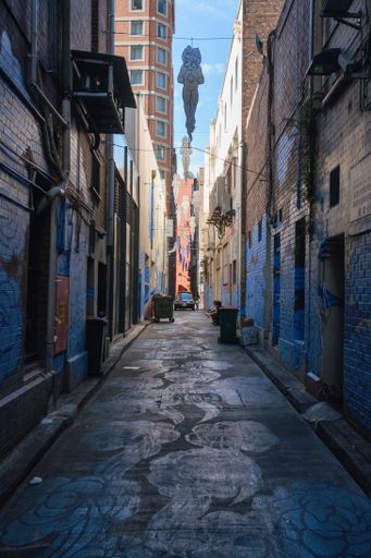 A vertical shot of a narrow walking street with garbage bins between buildings