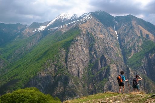 A view of a grand mountain and female hikers on a trail under a cloudy sky
