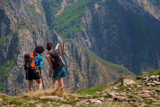 Two female hikers pointing and looking at a stunning view from a mountain top in Val Grande, Piedmont, Italy.
