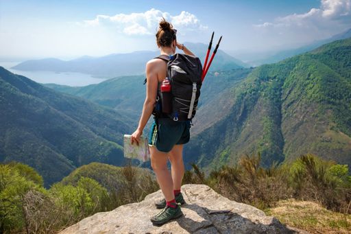 A high angle shot of a female hiking guide admiring the beautiful mountains  
with a map in her hand.