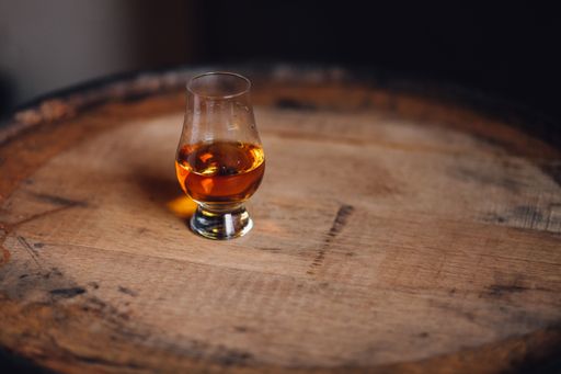 single Glencairn glass with dram of bourbon, scotch, rye on whiskey barrel